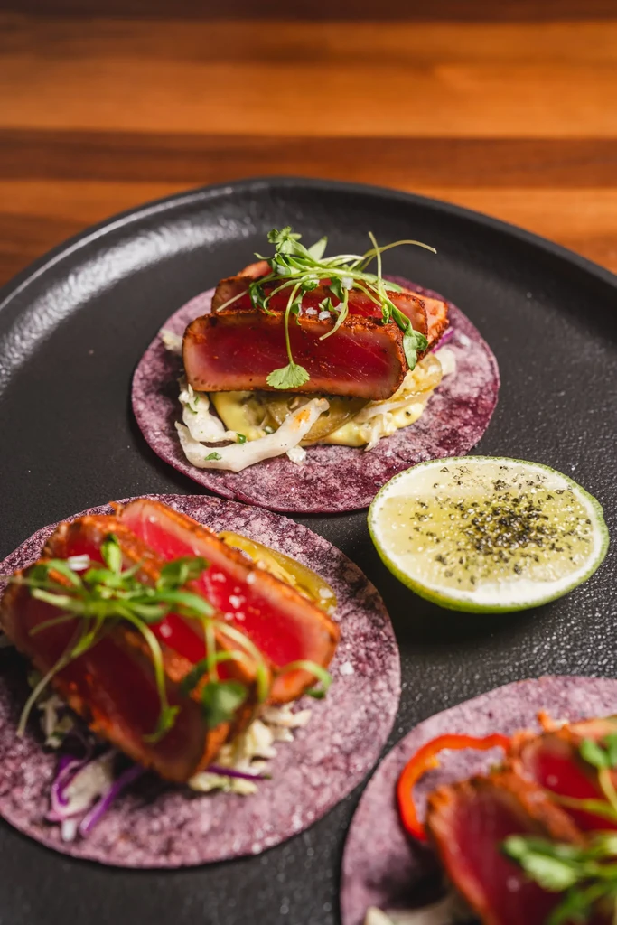 Three purple tortilla seared tuna tacos with slaw and seasoned lime.