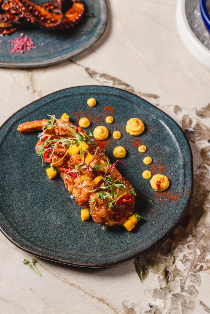 Professionally plated fried seafood garnished with mango, chili, and microgreens.