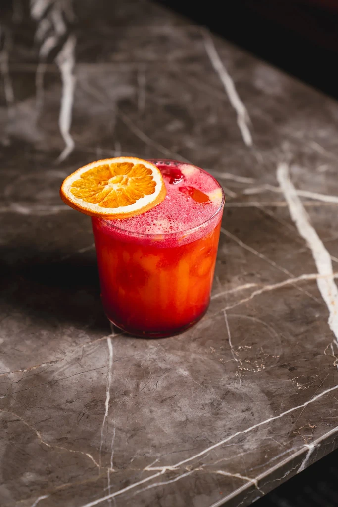 Layered orange and pink drink with a dried orange slice on dark marble.