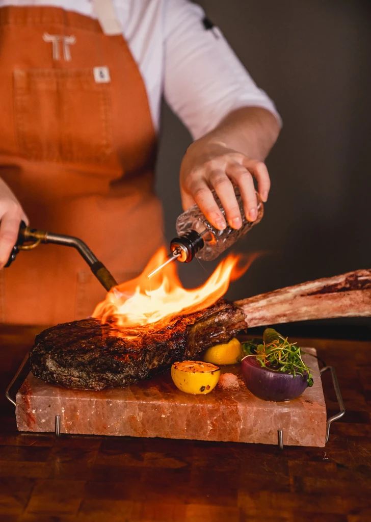 Chef torches a Tomahawk steak on a salt block with lemons.