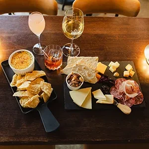 Charcuterie board, baked dip with chips, and three drinks on a table.