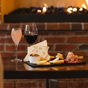 Charcuterie board with meats, cheeses, wines, fireplace background.
