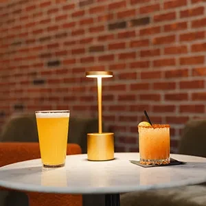 Drinks and illuminated lamp on marble table with brick wall.