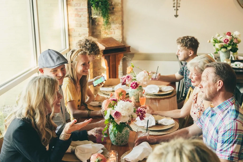 People enjoying lively conversation around a flower-decorated table.