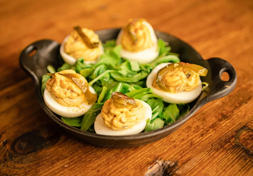 Five deviled eggs with jalapeño, paprika, and arugula in a rustic dish.