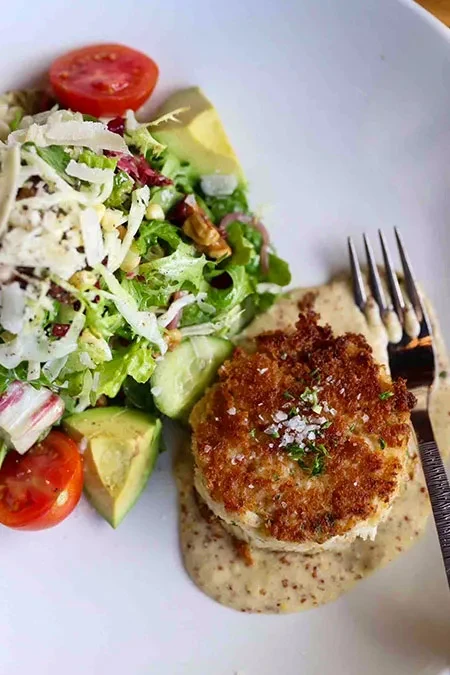 Golden-brown breaded patty on sauce with fresh salad and fork.