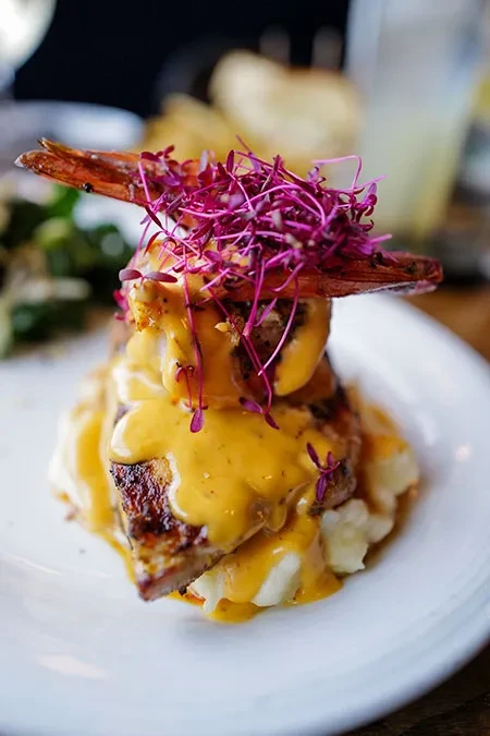Grilled protein stack with mashed potatoes, prawn, sauce, and microgreens.