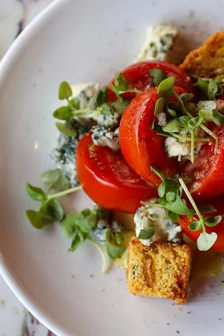 Close-up of plated tomatoes, blue cheese, microgreens, and croutons.