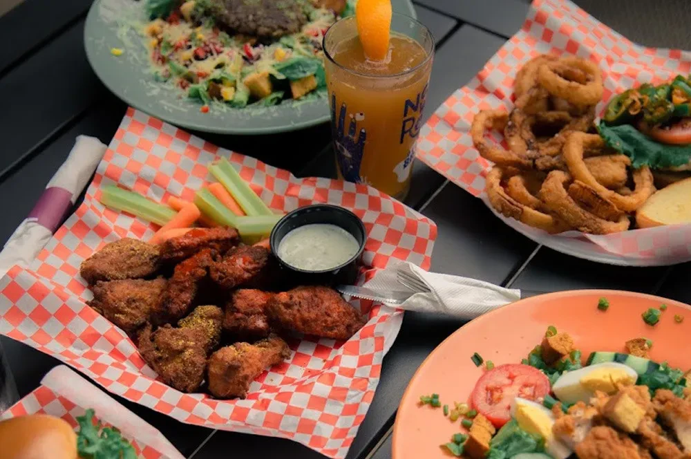 Top-down of table with chicken wings, onion rings, salads, and drinks.