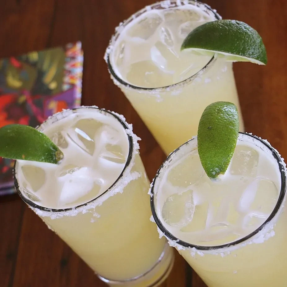 Three frosty margaritas with lime wedges and salted rims.