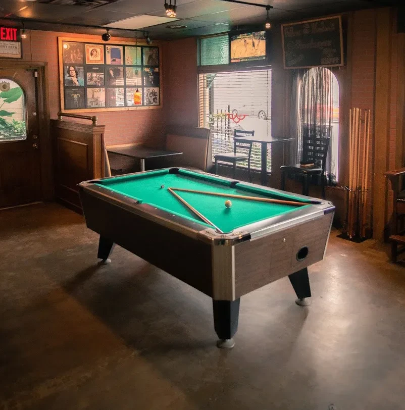Green pool table in a casual restaurant bar with booths and sports TV.