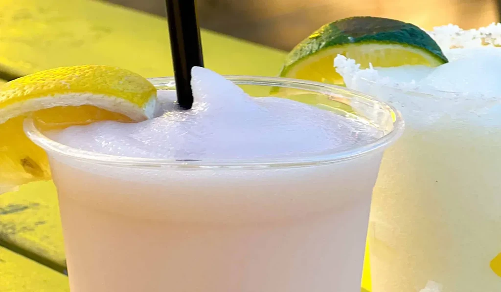 Pink slushy in plastic cup with lemon, a second drink with lime.