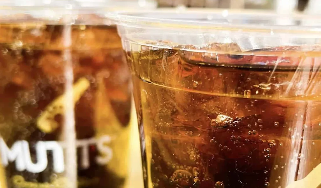 Two plastic cups with dark, fizzy drinks and ice, one says "MUTTS".