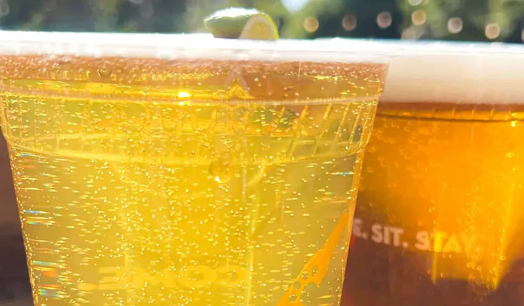 Two golden bubbly drinks in plastic cups, one with lime wedge.