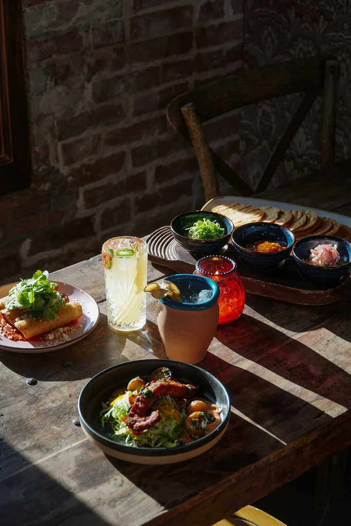 Rustic table with fried rolls, drinks, and salad in strong natural light.