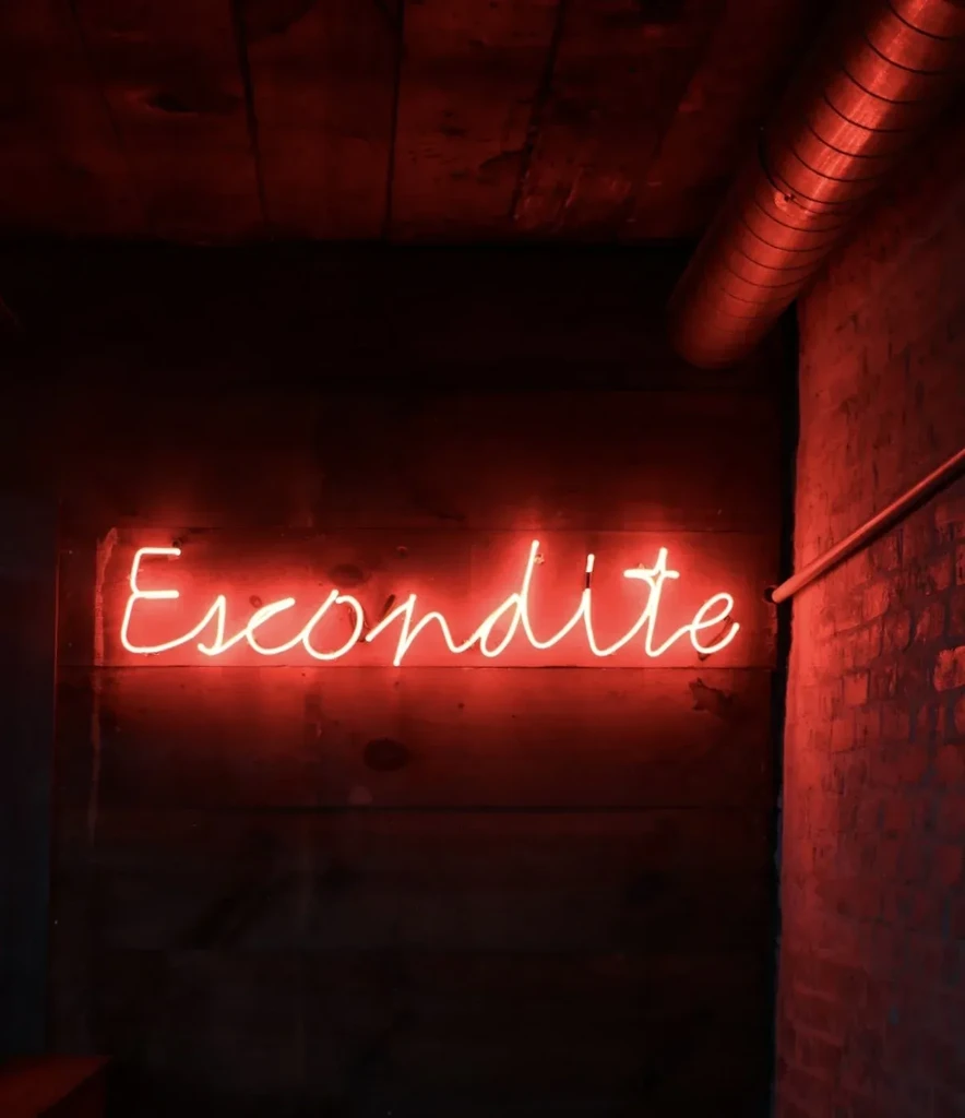 Red neon "Escondite" sign glowing on dark industrial background.