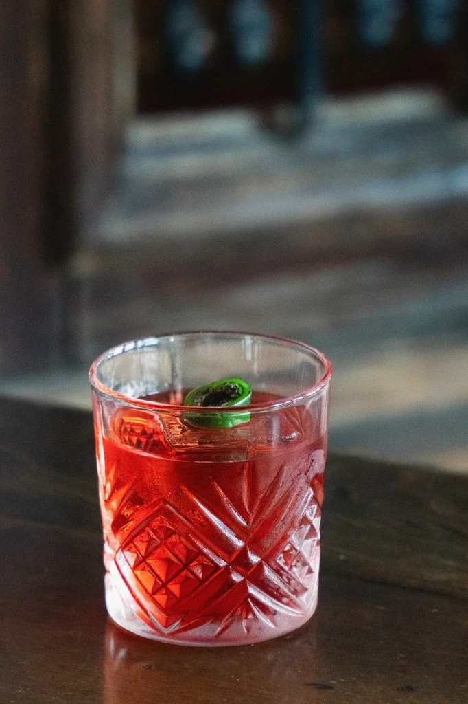 Vibrant red cocktail in a cold lowball glass with jalapeño.