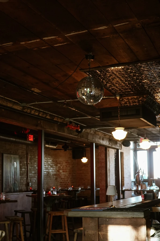 Dimly lit rustic bar with industrial wooden ceiling and prominent disco ball.