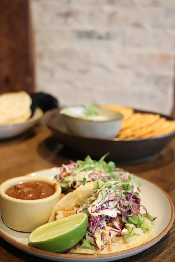 Two fish or chicken tacos with colorful coleslaw, salsa, and lime.