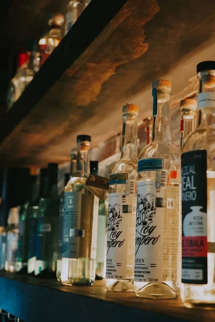 Close-up of labeled liquor bottles on a rustic wooden bar shelf.