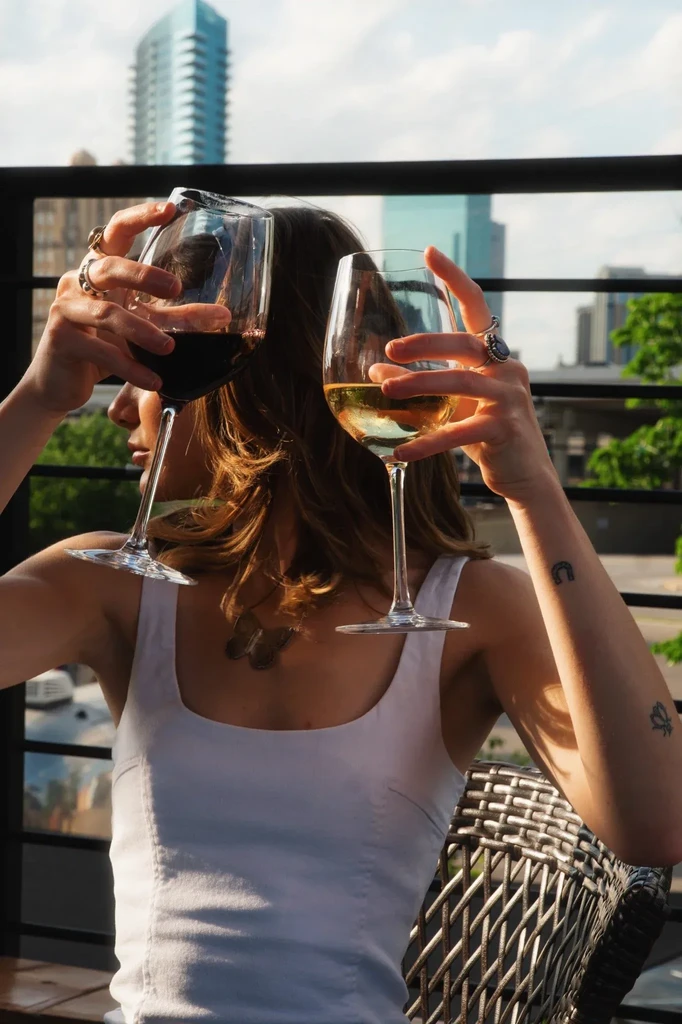 Person clinks red and white wine glasses, urban skyline.