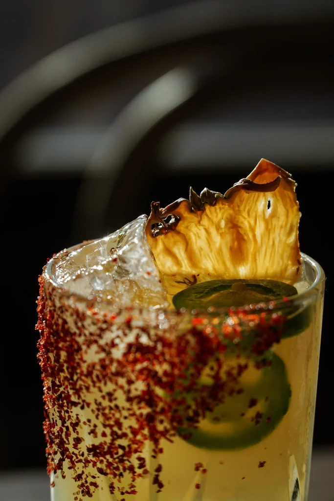 Cocktail with spicy rim, jalapeños, and dried pineapple slice.