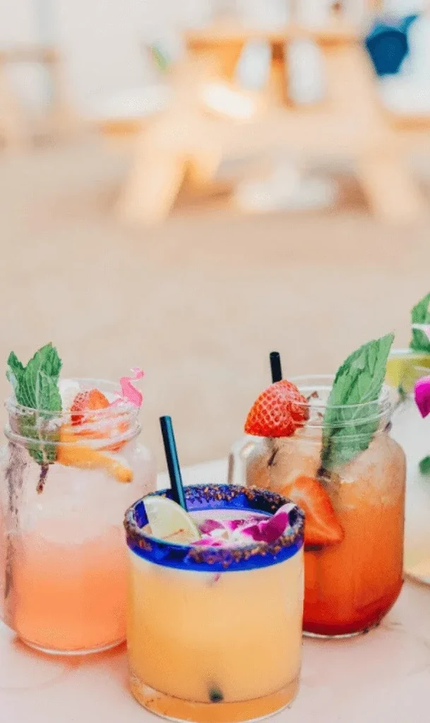 Three colorful, garnished beverages: pink, yellow, and orange.