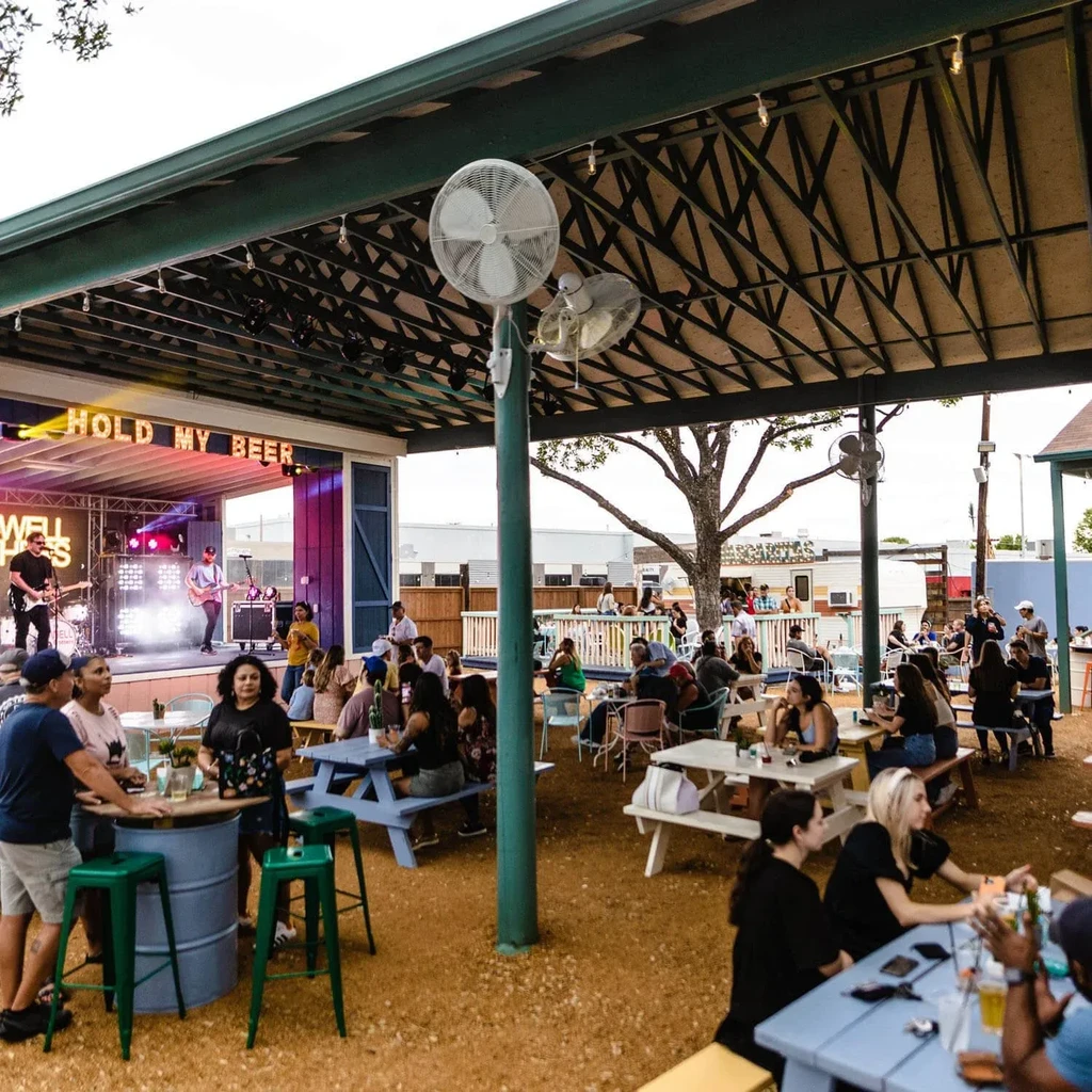 Lively outdoor beer garden with a band playing under 'HOLD MY BEER' sign.