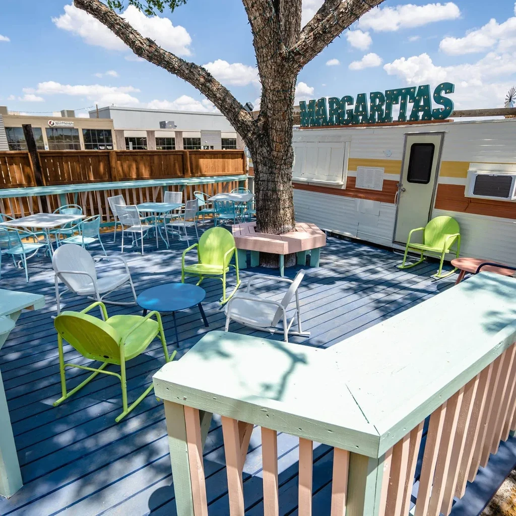 Outdoor blue deck patio with tree, colorful seating, and "MARGARITAS" sign.