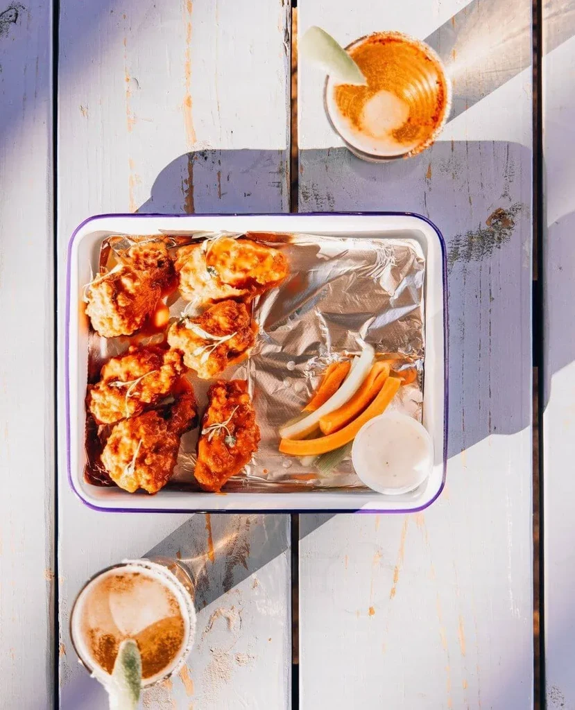 Tray of fried chicken, vegetables, and two garnished drinks outdoors.
