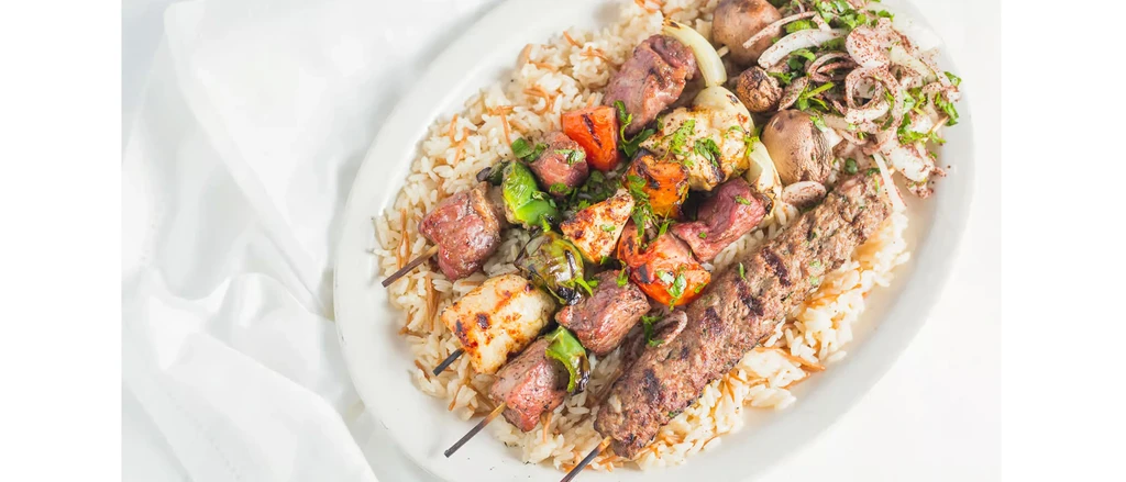 Grilled chicken, beef, and kofta skewers with vegetables over rice.