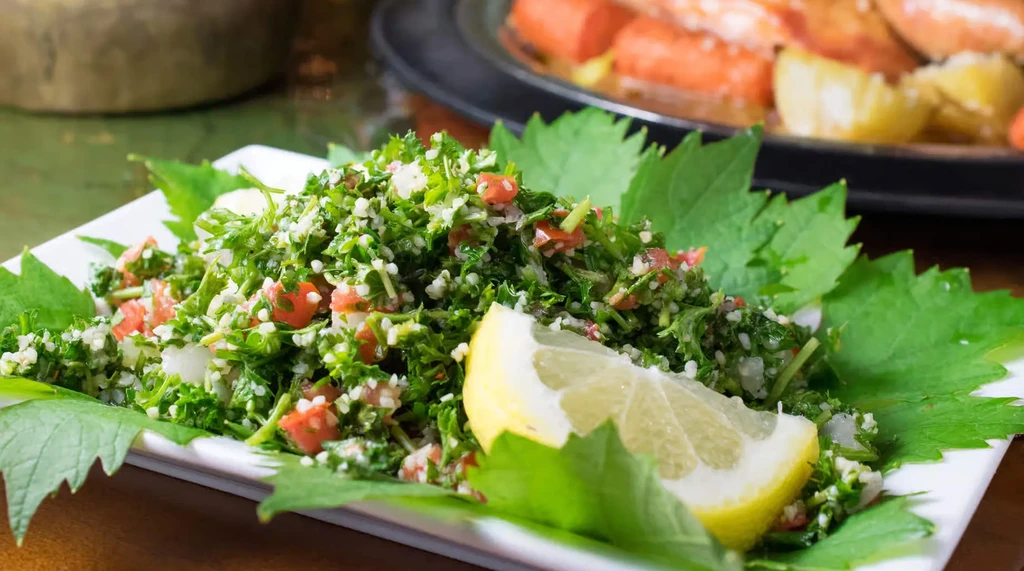 Fresh herb salad with tomatoes and lemon on a white plate.