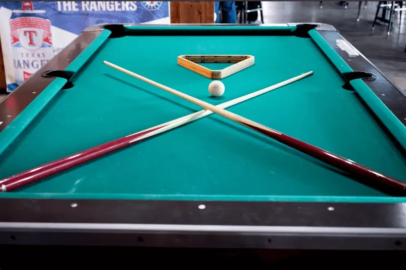 Green pool table with crossed cues, white cue ball, and triangle rack.