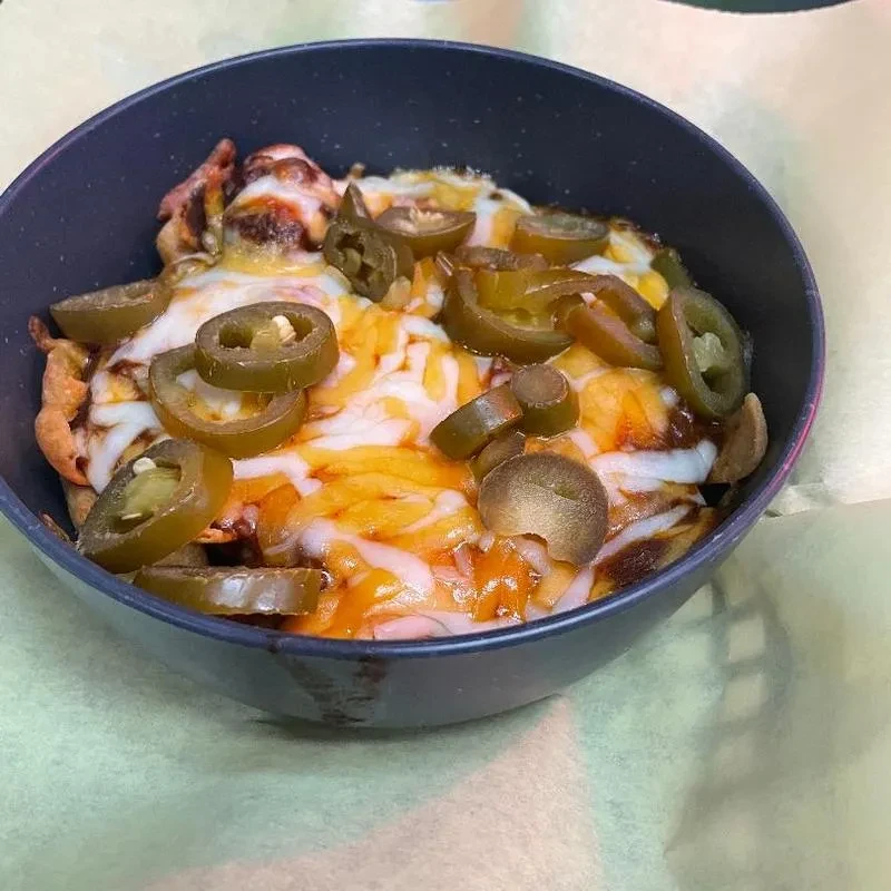 Dark bowl of nachos with melted cheese and pickled jalapeños.
