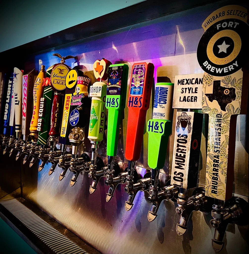 A row of 15-20 unique beer taps with logos and colorful light.