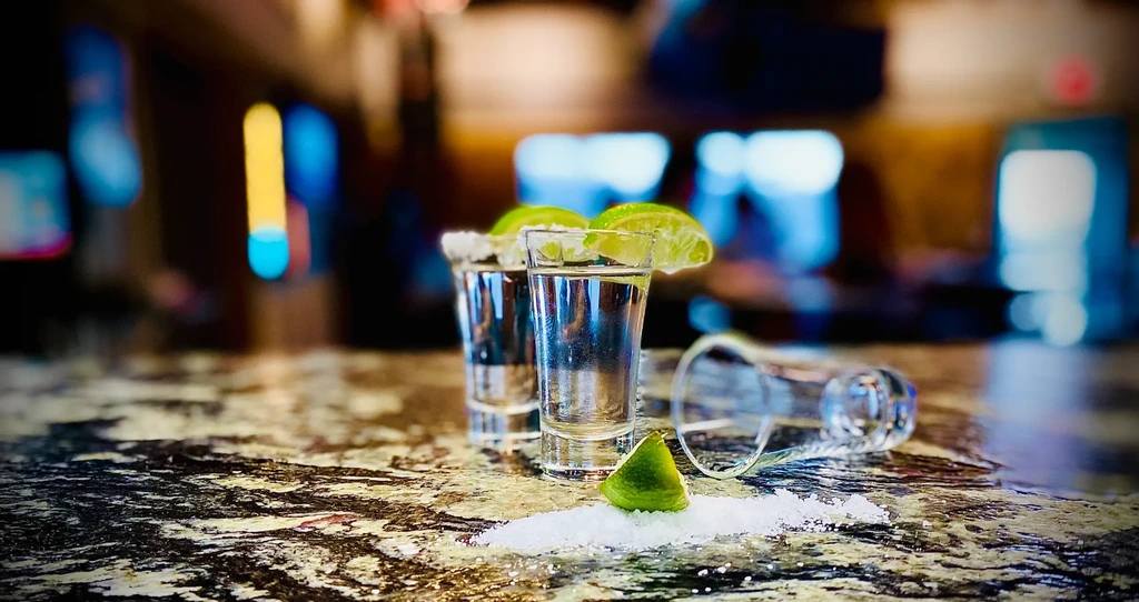 Two tequila shots with lime and salt on a dark counter.