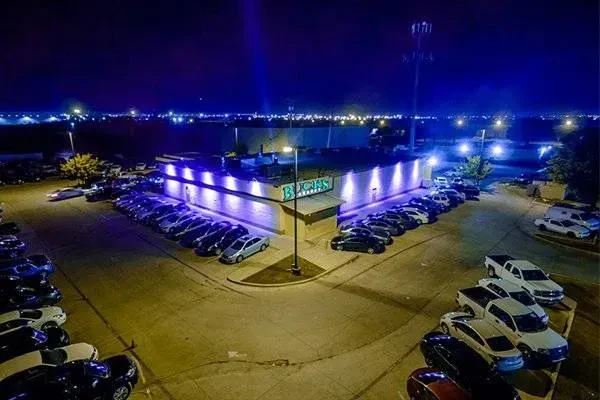 Aerial night view of BUCKS building, blue-lit, with a crowded parking lot.