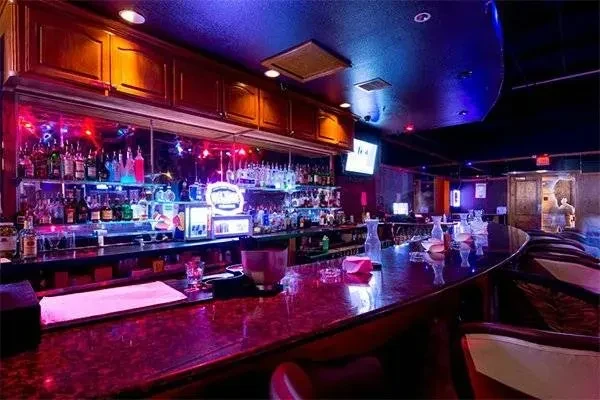 Colorful, dimly lit bar with a curved counter and stocked liquor bottles.