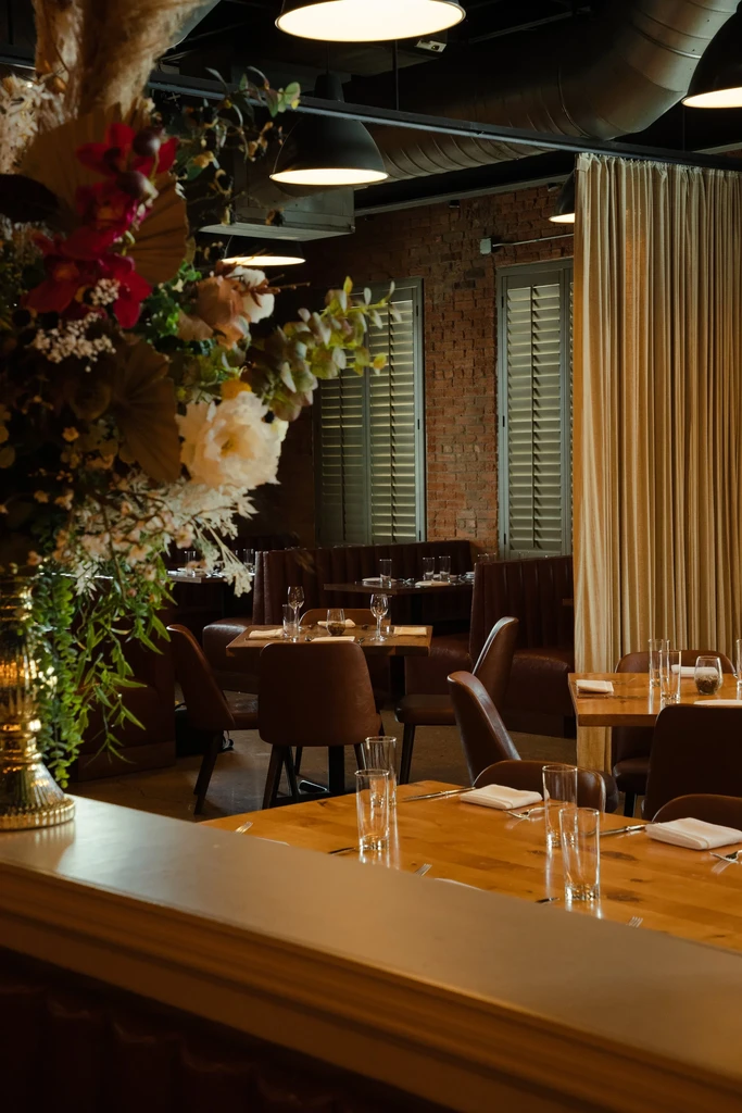 Empty sophisticated restaurant interior with brick walls, tables, and floral vase.