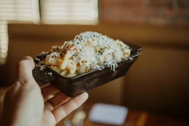 Mac and cheese topped with grated cheese and herbs, held by a hand.