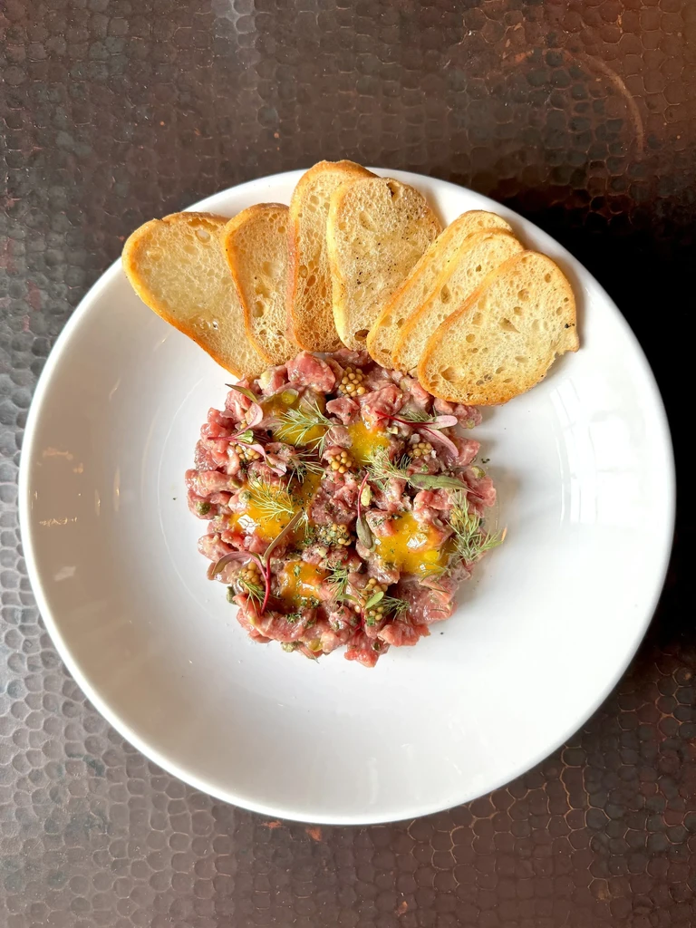 Close-up steak tartare with two egg yolks, dill, and crostini.