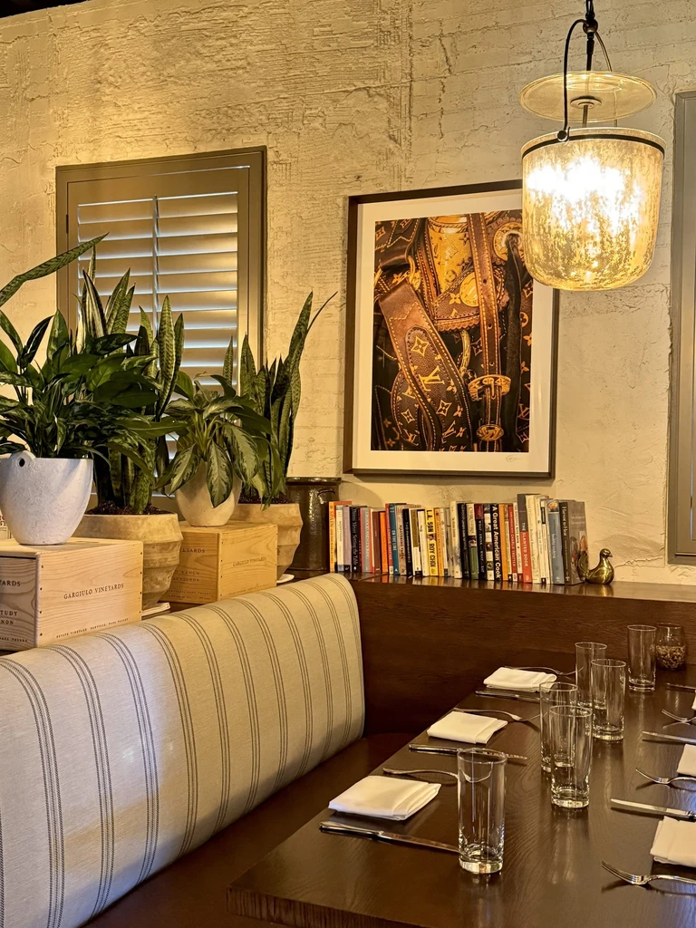 Warm restaurant interior with plants, set table, and LV monogram artwork.
