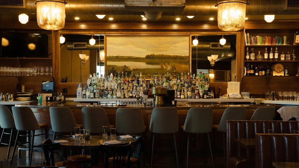 Restaurant bar with extensive liquor bottles, hunting painting, and patterned stools.