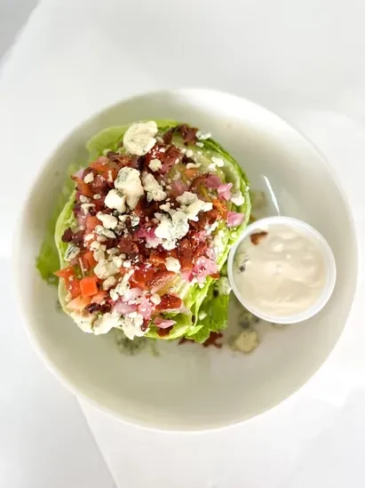 Iceberg wedge salad topped with blue cheese, bacon, tomato, red onion, dressing.