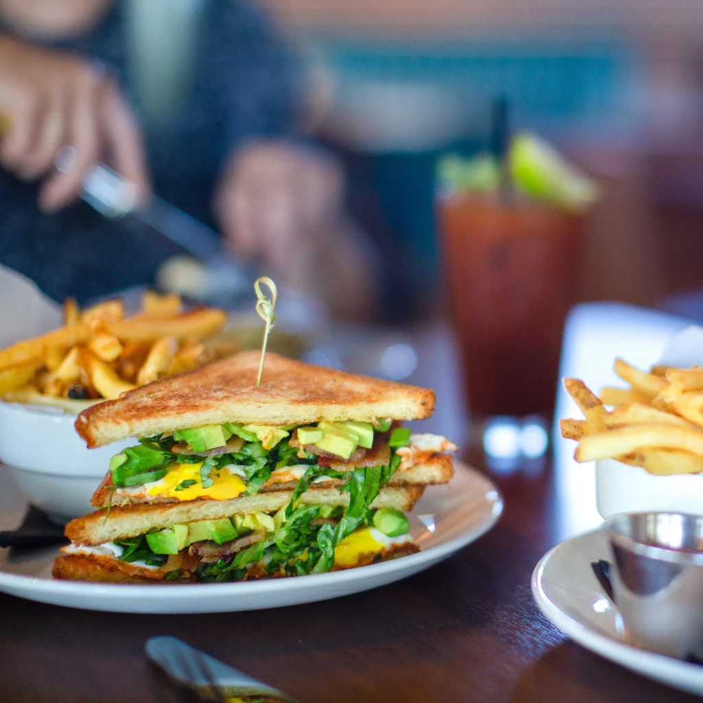 Layered club sandwich with avocado, bacon, eggs, and french fries.