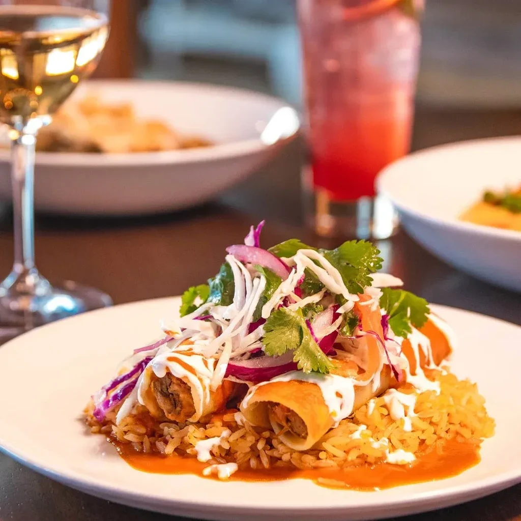 Two golden taquitos on yellow rice, topped with vegetables and crema.