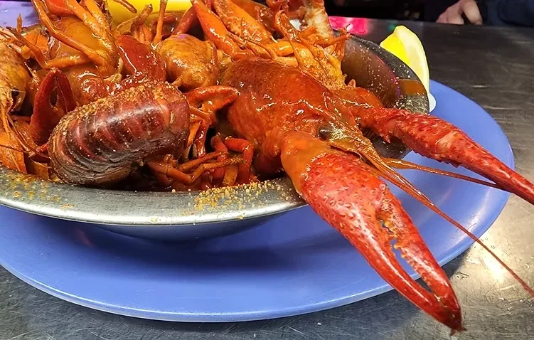 Piled high red and orange crawfish and lemon in a metal bowl.