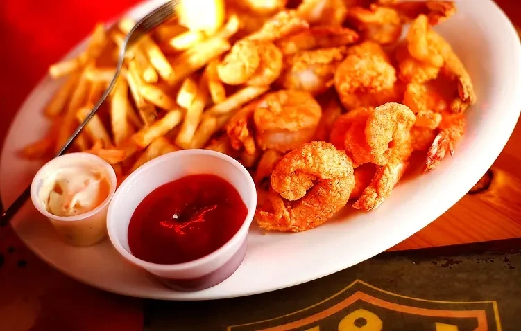 Close-up of crispy fried shrimp, golden fries, tartar, and ketchup.