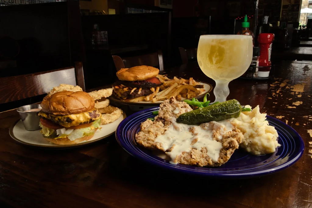 Two burgers, chicken fried steak, fries, and a beer on a wooden table.