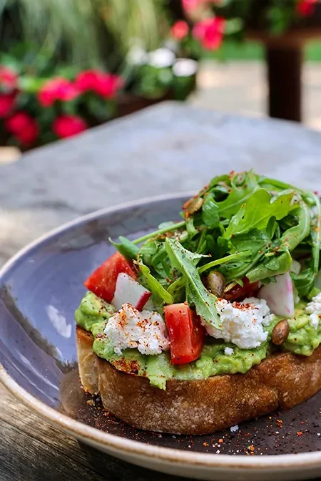 Close-up of avocado toast with arugula, tomatoes, cheese, radish, pumpkin seeds.
